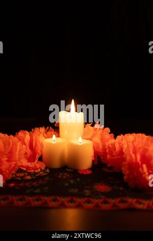 Une photo verticale avec trois bougies allumées au centre de l'image, entourées de soucis orange vifs. La scène est éclairée par des chandelles Banque D'Images