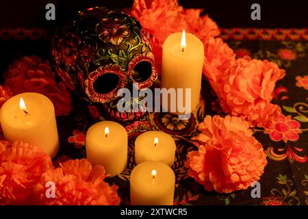 Gros plan d'un crâne décoré d'accents floraux métalliques, entouré de fleurs de souci orange. Cinq bougies éclairent la scène, avec un jour des morts Banque D'Images