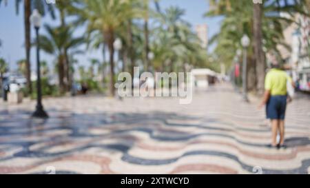 Vue floue de la promenade extérieure à alicante, espagne avec des gens en arrière-plan, des palmiers et un pavé à motifs sous un ciel bleu clair. Banque D'Images