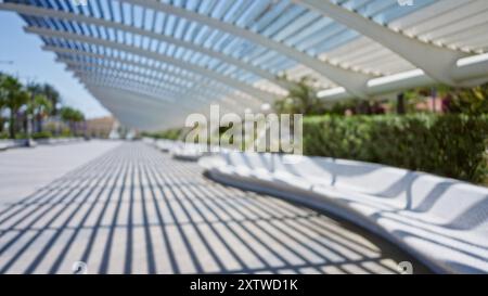 Scène extérieure floue avec effet bokeh flou avec un banc moderne sous une structure architecturale et des palmiers en arrière-plan Banque D'Images