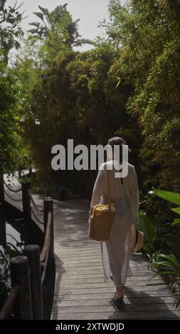 Une jeune femme se promène dans un sentier balinais luxuriant, incarnant la tranquillité et les loisirs dans un cadre tropical. Banque D'Images