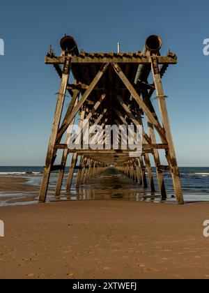 La vieille structure de jetée en bois disparaît dans la mer à marée basse, créant un point de fuite Banque D'Images