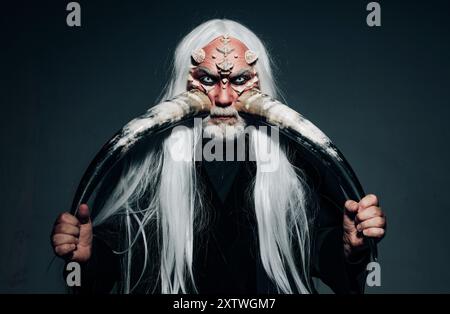 Homme âgé tenant deux cornes rouges. Tête de démon isolée sur noir. Alchimie ancienne. Cornes de diable. Vieux barbu habillé comme un monstre d'Halloween. Druide Banque D'Images