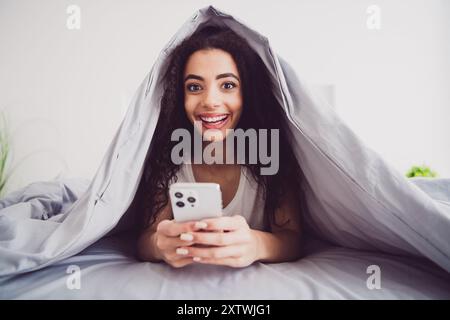 Photo de charmante jeune femme couchée lit couvert couverture dispositif de maintien Good Morning vibes éveillé maison chambre lumière intérieur blanc Banque D'Images