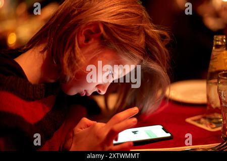 Une jeune fille a été englouti dans l'utilisation de son smartphone avec une lumière chaude illuminant son visage. Banque D'Images