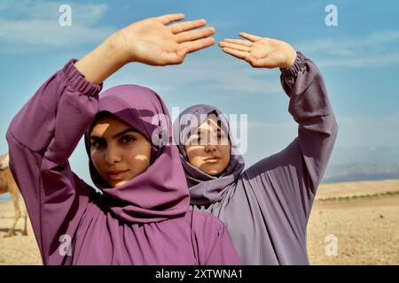 Deux femmes en hijabs posant avec leurs mains encadrant le ciel dans un paysage désertique. Banque D'Images