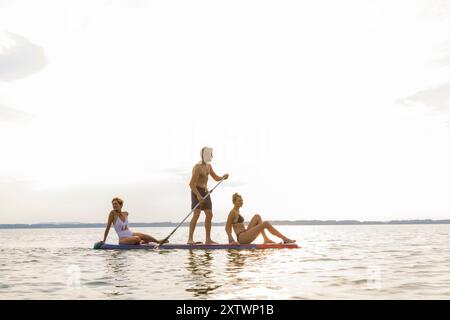 Trois amis apprécient le paddleboard sur un lac serein lors d'un coucher de soleil. Banque D'Images