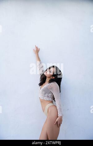 Une jeune femme aux longs cheveux bruns pose dans un cadre de studio, portant un haut en tricot blanc. Banque D'Images