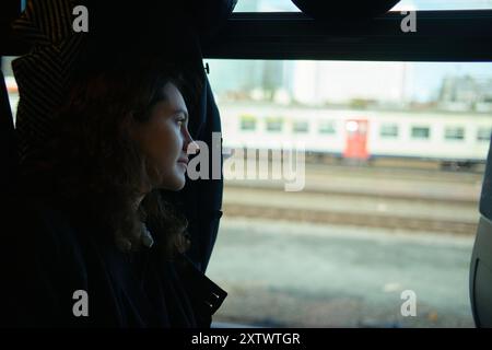 Une jeune femme regarde par la fenêtre d'un train, observant le paysage pendant que le voyage se déroule. Banque D'Images