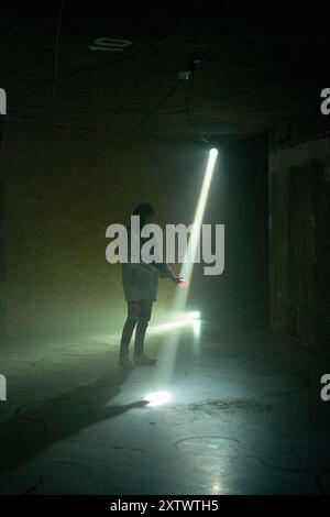 Personne silhouette debout dans une pièce sombre illuminée par un puissant faisceau de lumière provenant d'une ouverture. Banque D'Images