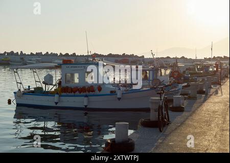 Coucher de soleil illumine un port serein avec des bateaux de pêche amarrés reflétant sur l'eau calme. Banque D'Images