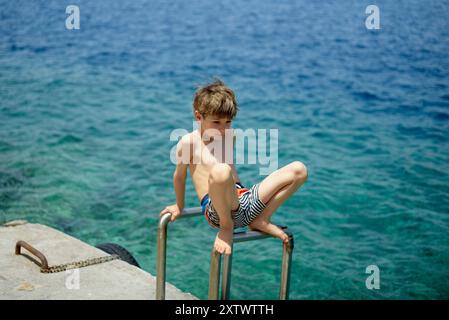 Garçon en maillot de bain se préparant à plonger dans l'océan depuis une corniche rocheuse. Banque D'Images