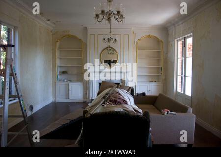 Une chambre spacieuse en cours de rénovation avec des meubles recouverts de toiles de chute, une échelle dans le coin, et du papier peint partiellement dépouillé. Banque D'Images