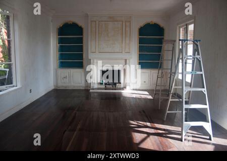 Chambre vide lors de la rénovation avec échelle, parquet foncé, cheminée et étagères intégrées. Banque D'Images
