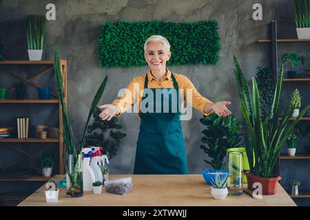 Photo de Shiny Happy Age femme habillé tablier vous invitant à rassembler des plantes à l'intérieur de l'atelier à la maison Banque D'Images