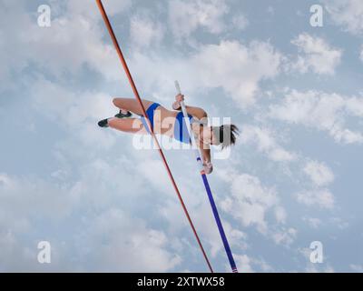 Athlète féminine voûtant au-dessus d'une barre haute contre un fond de ciel nuageux. Banque D'Images