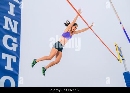 Athlète féminine sautant par-dessus une barre haute dans une compétition de voûte à la perche avec joie et athlétisme. Banque D'Images