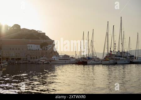Le coucher du soleil brille derrière une forteresse perchée surplombant une marina sereine bordée de voiliers amarrés. Banque D'Images
