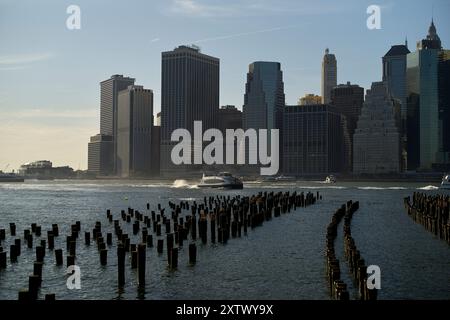 Vue sur le coucher du soleil de la ville de New York avec des restes de jetée silhouette au premier plan et des bateaux sur l'eau. Banque D'Images