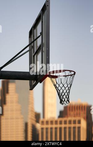 Panier de basket-ball en plein air avec un panneau clair sur fond de gratte-ciel de la ville pendant le coucher du soleil. Banque D'Images