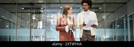 Deux collègues discutent dans un hall de bureau moderne, l'un tenant une tasse de café et l'autre examinant un document. Banque D'Images