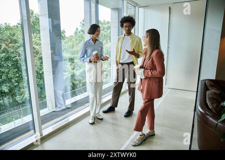 Trois collègues, dont une femme avec une prothèse de jambe, se tiennent près d'une fenêtre dans un bureau moderne, engagés dans une conversation amicale. Banque D'Images
