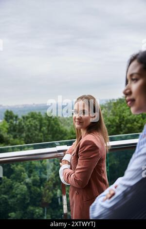 Deux collègues divers se tiennent sur une terrasse sur le toit, discutant et profitant de la vue. Banque D'Images