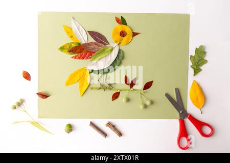 un projet artisanal où diverses feuilles et matériaux végétaux sont disposés sur un fond de papier vert pour ressembler à un oiseau. projet écoliers. vue de dessus. a Banque D'Images