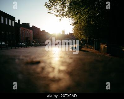 La lueur chaude du coucher de soleil projette une lumière douce sur les bâtiments historiques entourant une place paisible de la ville. L'atmosphère se sent tranquille comme le jour tr Banque D'Images