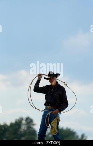 Cow-boy en chapeau noir tient un lasso contre un fond de ciel nuageux. Banque D'Images