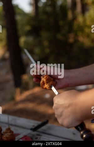 Gros plan des mains des hommes enfiler la viande de porc sur une brochette Banque D'Images