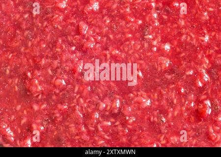 Cette image en gros plan vibrante met en valeur la texture riche des framboises naturelles écrasées. Le mélange de teintes rouges et roses met en valeur la fraîcheur du fr Banque D'Images