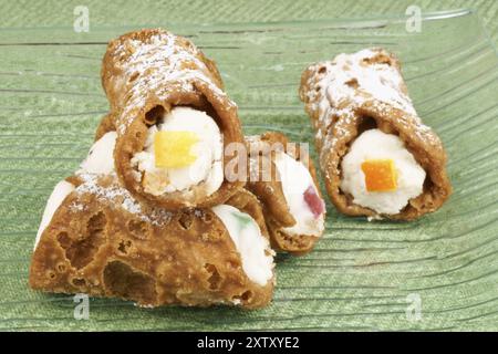 Gros plan de mini cannoli siciliens originaux sur une plaque de verre transparente sur un fond vert. Ces pâtisseries en forme de tube sont faites de coquilles frites f Banque D'Images