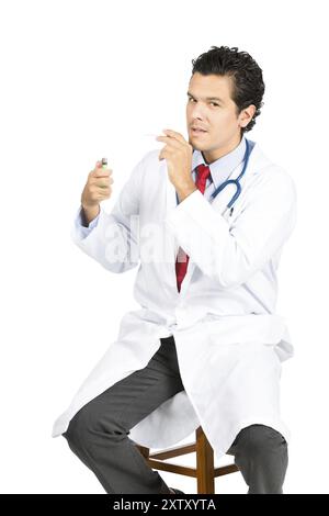 Un médecin latino en blouse de laboratoire blanche, stéthoscope allumant ironiquement une cigarette contre les conseils médicaux regardant la caméra. Profil latéral V Banque D'Images