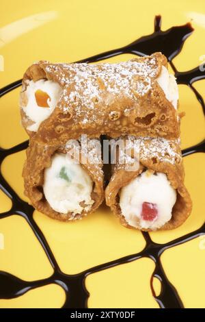 Gros plan de mini cannoli siciliens originaux sur une plaque jaune. Ces pâtisseries en forme de tube sont faites de coquilles frites remplies d'un mélange sucré de riques Banque D'Images