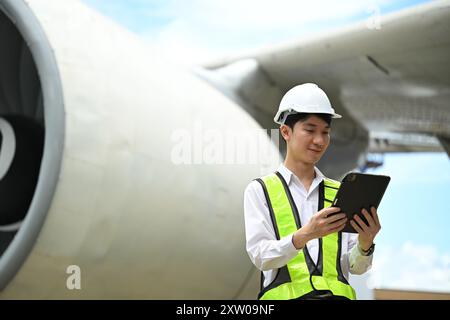 Jeune ingénieur masculin ou technicien aéronautique utilisant une tablette numérique devant un gros moteur d'avion Banque D'Images