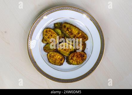 Gourde épineuse (Momordica dioica) frite ou kakrol bhaja dans une plaque blanche sur une surface en bois clair. Il est également connu sous le nom de gourde épine, kantola, kartoli, bhat k Banque D'Images