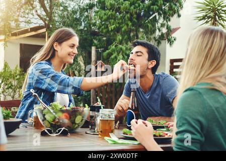 En plein air, alimentation et femme avec salade, homme et rassemblement pour les réunions avec des amis, arrière-cour ou manger. Maison, mains et bol de nourriture en week-end, cour Banque D'Images