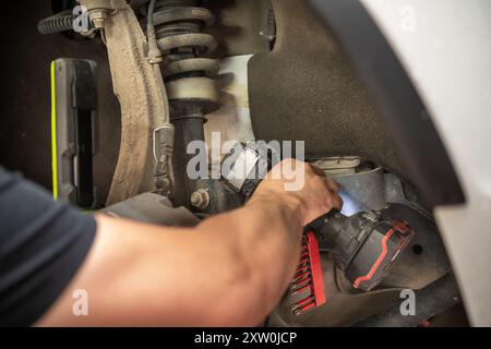 Un mécanicien se concentre sur la réparation du système de suspension d'une voiture, en utilisant un outil électrique pour assurer la précision dans l'environnement du garage. L'ex du mécanicien Banque D'Images