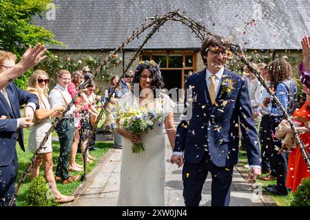 Mariée et mariée marchent de la cérémonie de mariage avec des invités jetant des confettis. Banque D'Images