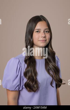 Jeune fille brune adolescente sérieuse avec des bretelles et des taches de rousseur dans un cadre de studio pour un tir de tête sur un fond brun beige Banque D'Images