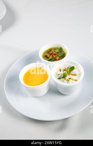 Différentes sauces savoureuses dans des bols sur une table blanche, plat. Restaurant style légumes Raita et Chutney vert, yaourt épicé menthe Chutney (Pudina Raita) Banque D'Images