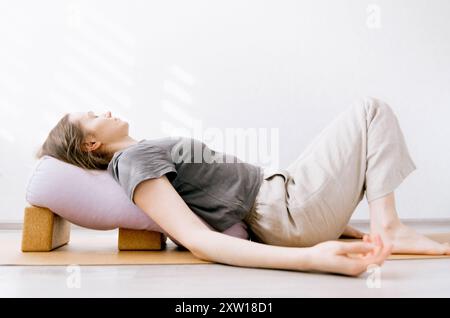 Femme en vêtements décontractés faisant du yin / yoga réparateur avec traversin soutenu par des blocs Banque D'Images