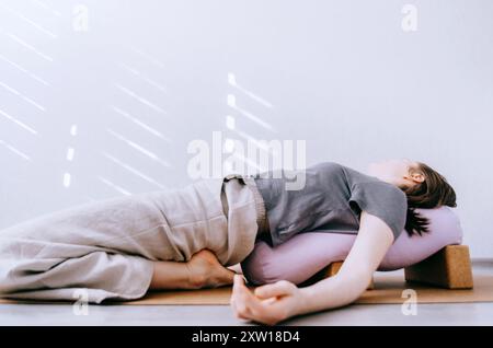 Femme en vêtements décontractés faisant du yin / yoga réparateur avec traversin soutenu par des blocs Banque D'Images