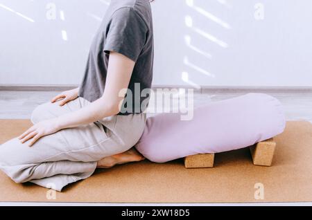 Femme en vêtements décontractés faisant du yin / yoga réparateur avec traversin soutenu par des blocs Banque D'Images