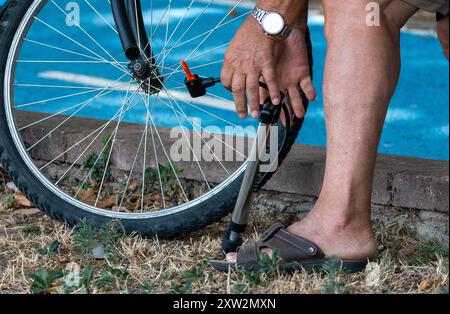 Perspective rapprochée : vieil homme gonflant manuellement son pneu de vélo dans le parc. Banque D'Images