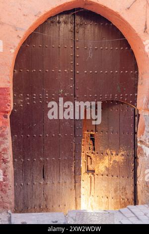 Grande entrée de voiture fermée, dont seule une petite porte semi-ouverte laisse passer la lumière d'un soleil matinal Banque D'Images