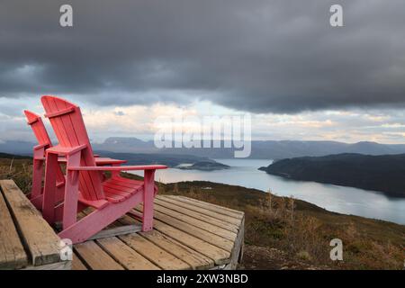 Deux chaises adirondack rouges sur une terrasse en bois surplombant bonne Bay ; Terre-Neuve-et-Labrador, Canada Banque D'Images