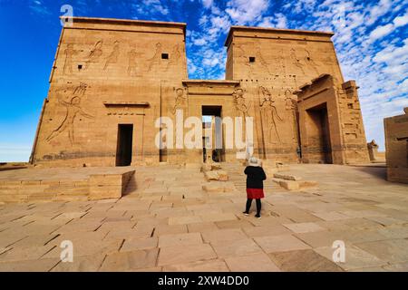 Un visiteur admire les magnifiques reliefs muraux représentant Ptolémée au pylône d'entrée du temple d'Isis à Philae Island sur le lac Nasser, construit par Nectanebo et Ptolémée Pharoahs près d'Assouan, en Égypte Banque D'Images