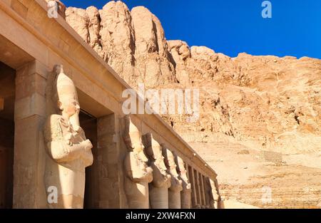 Des statues massives de la Grande femme Pharoah Hatshepsout avec l'escroc et le fléau en tant que souverain de l'Égypte sculpté dans le grès dominent les colonnes extérieures du Temple mortuaire près de Louxor, en Égypte Banque D'Images